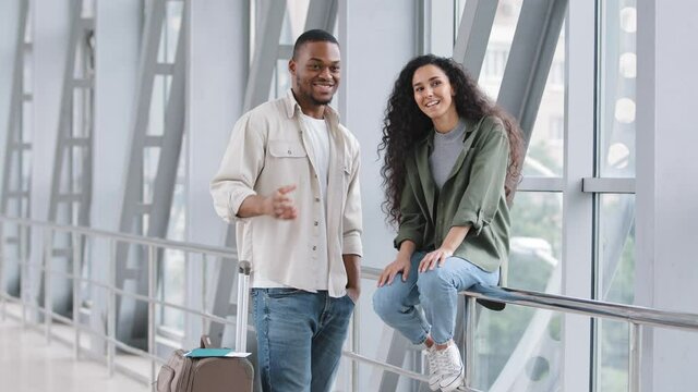 Multiracial couple hispanic woman and african man sitting standing at airport with suitcase talking conversation showing hands direction in front of them talk before boarding plane honeymoon travel