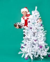 Handsome cheerful man in a New Year's hat and with a white artificial Christmas tree on a green background