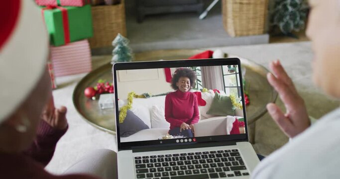 Diverse senior female friends waving and using laptop for christmas video call with woman on screen