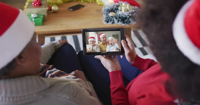 African american mother and daughter using tablet for christmas video call with family on screen