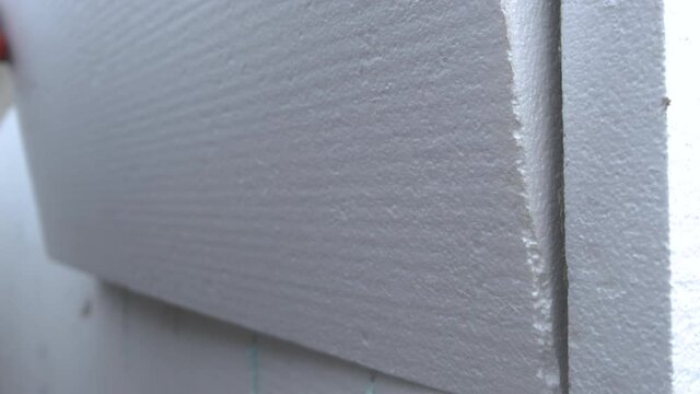 Construction worker installing styrofoam insulation sheets on house facade wall for thermal protection.