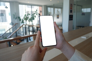 Mockup picture of business woman’s hands holding smart phone with white blank screen in modern place