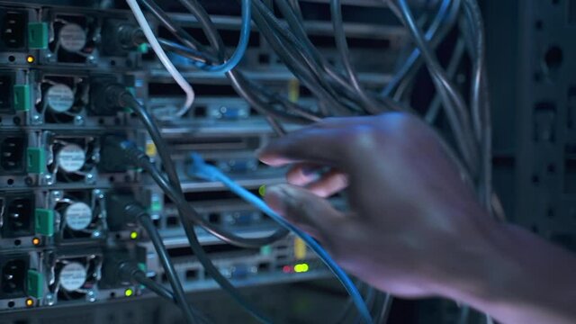 Engineer specialist works in server room. African-American employee switches cables fixing network equipment spbas on rack in semi-dark data center closeup - Powered by Adobe