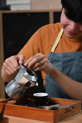 Fototapeta na wymiar Smiling asian man pouring coffee from moka pot coffee maker to small coffee cup.