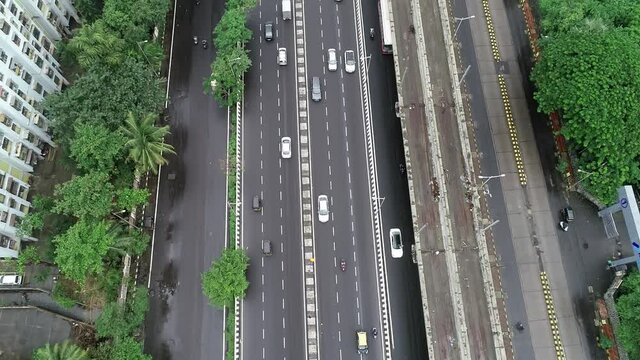 Top aerial drone revealing shot from a busy six lane Highway with fast-moving vehicles to urban skyscrapers or modern landscape of Metropolitan or Megacity during broad daylight