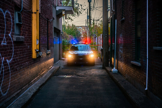 Police car in a dark alley in Montreal, Canada with flashing red and blue lights
