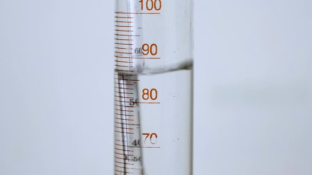 An alcoholic alcohol meter floats in a flask into which drops of alcohol from a moonshine apparatus still fall. Closeup