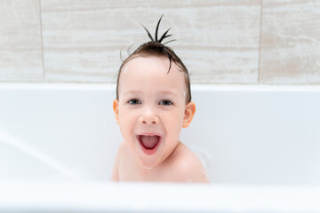 A happy little boy is playing in a bubble bath. A small child in the bathtub, a smiling child in the bathroom, Hygiene and care for young children.