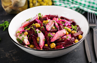 Salad with herring, green peas and beetroot filled with vegetable oil on a dark table.
