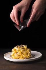 Tagliatelle pasta with black truffle. Female hands grating  black truffle. Italian autumn pasta ...