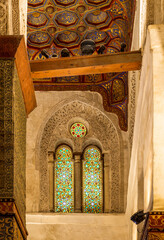Two adjacent perforated stucco arched windows decorated with colorful stain glass with geometrical...
