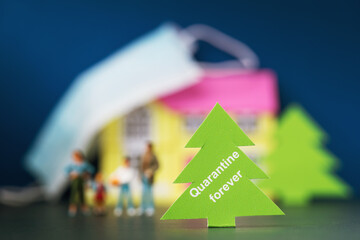 Christmas tree made of paper with text on the background of a blurred toy house, people and a medical mask, the concept of quarantine forever