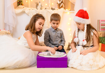 children celebrating christmas or new year, drink tea, eat cookies and play with the toy dishes in home interior decorated with holiday lights and gifts
