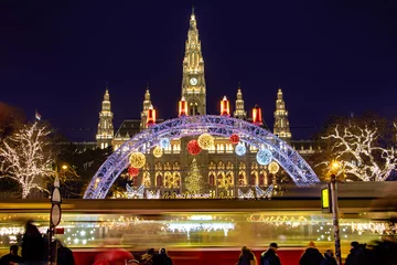 Deurstickers The tram is ride in front of the Christmas market by City hall -  Rathaus in night Vienna, Austria. © milkovasa