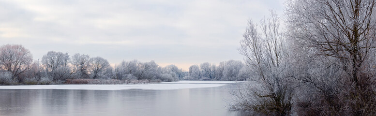 Frost-covered trees on the banks of an ice-bound river in the morning during sunrise