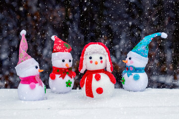 Cheerful snowmen in the forest on a dark background during a snowfall. Christmas and New Year greeting card