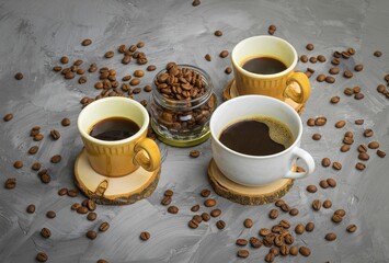 There are three cups on a wooden round stand, in which there is black coffee with sugar, there are a lot of coffee beans nearby