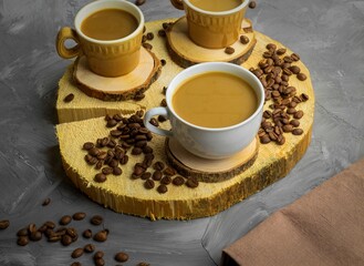There are three cups on a wooden round stand, in which coffee with milk is poured, there are a lot of coffee beans next to it