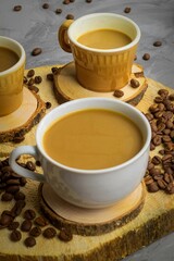 There are three cups on a wooden round stand, in which coffee with milk is poured, there are a lot of coffee beans next to it