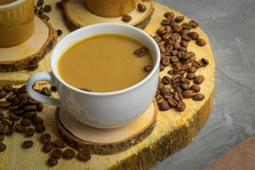 There are three cups on a wooden round stand, in which coffee with milk is poured, there are a lot of coffee beans next to it