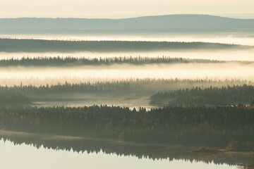 Beautiful fells in fog during a calm morning by a lake in Northern Finland near Kuusamo in autumn.