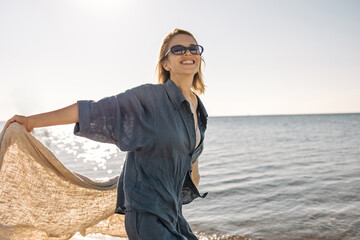Happy caucasian young lady smiles broadly against background of blue sea. Short-haired blonde in...