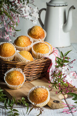 still life of delicious golden cupcakes in a wicker basket decorated with flowers and an antique coffee pot. home made
