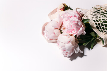 pink peony flowers in a string bag on a white background