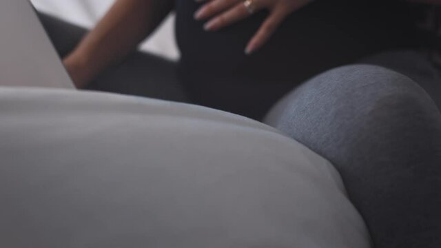 4K footage of a pregnant girl lying on the bed plays with her computer
