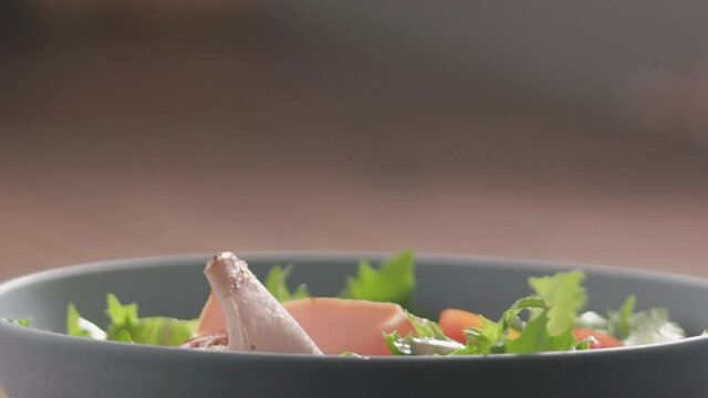 Slow motion turkey slices fall on green frisee lettuce in blue bowl closeup