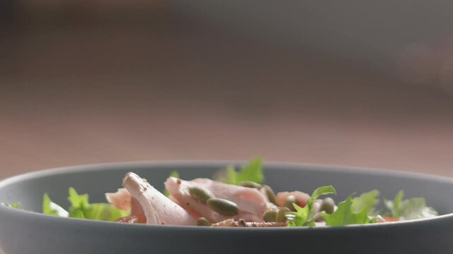 Slow motion pumpkin seeds fall on green frisee lettuce in blue bowl closeup