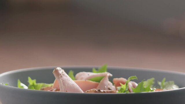 Slow motion turkey slices fall on green frisee lettuce in blue bowl closeup