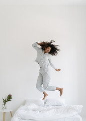 Mixed race woman jumping over bed in morning