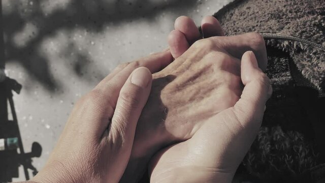 Younger adult woman holding elderly woman's hand.