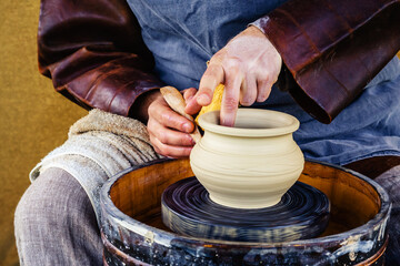 An old-fashioned potter creates a clay pot. The process of work of a master on a mechanical, wooden machine. Close-up. Unrecognizable person