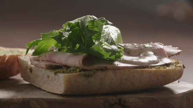 Slow motion put lettuce over turkey slices on ciabatta to make sandwich