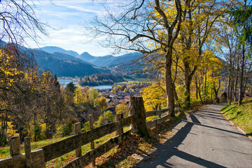 Narrow mountain road with a beautiful view of a lake as a background during Autumn. Road arround Schliersee lake during Fall and a view of the city in german Alps, Bavaria, Germany