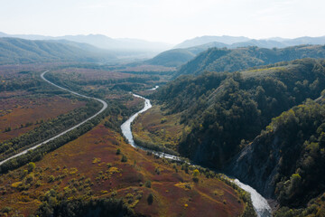 Mountain road and winding river in  mountains gorge, autumn landscape, red leaves, aerial drone view