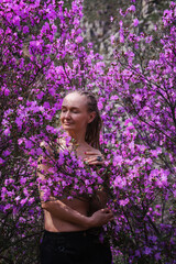 Portrait of Woman in Altai mountains walking among beautiful pink Rhododendron flowers. Spring mountain landscape