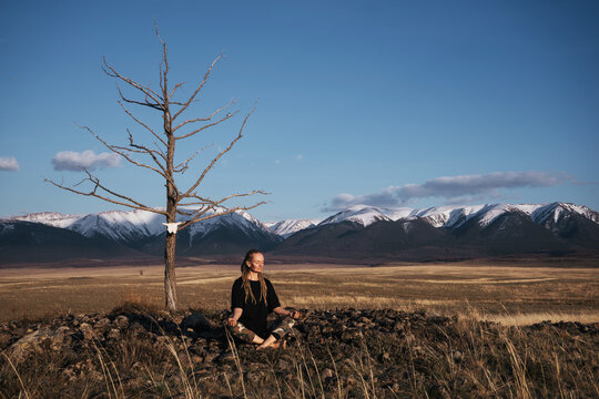 Woman sitting under dry tree meditating in Altai mountains