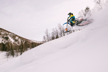 Snowbike female rider jumping in mountain valley. Modify dirt bike with snow splashes and trail. Snowmobile sport riding
