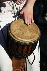 Hands are tapping on an African drum. A sunny summer day. Fingers and nails. A brown drum in a mesh. Warm and sunny