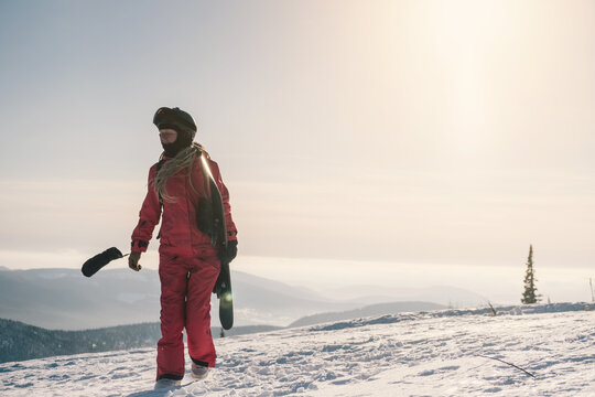 Female with snowboard. Snowboarder walking on snowy slop watching beautiful atmospheric mountain landscape