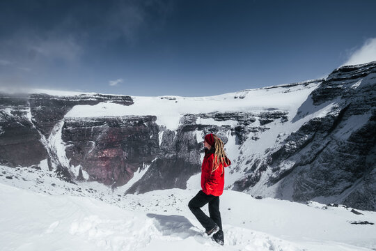 Female traveler standing near Crater of the Tolbachik volcano, snowy peak of summit and crater