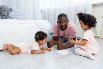 african-American dad teaches kids how to draw pencils on the floor at home