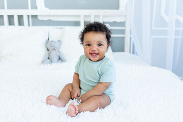 African-American baby smiles or laughs while sitting on the bed at home