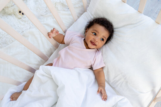 african american baby boy in the crib goes to bed or wakes up in the morning and smiles in the bedroom