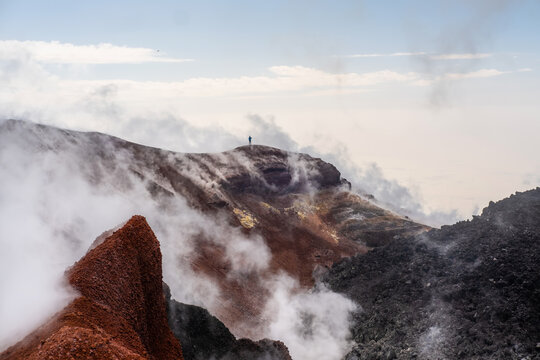 man standing on the crater of active volcano. Red earth, gas, steam