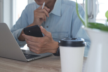 Asian business man using mobile phone, thinking about his work project during working on laptop...