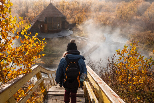 Woman at hot spring. First frost, hot water, beautiful wooden house in colourful autumn landscape